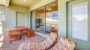 Un patio con mesa y sillas, un rincón de estar con cojines y un ventanal corredero que da a un espacio interior.