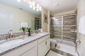 Une salle de bain moderne avec un comptoir en granit, deux lavabos, une cabine de douche en verre et des toilettes.