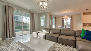 A spacious living room with a sectional sofa, a glass coffee table, and a chandelier. - Champions Gate Home 2 U- Maui- Cg1560 (Davenport)