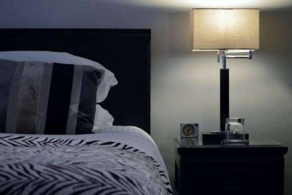 A neatly made bed with a patterned bedspread, a bedside table with a lamp, and a small clock.