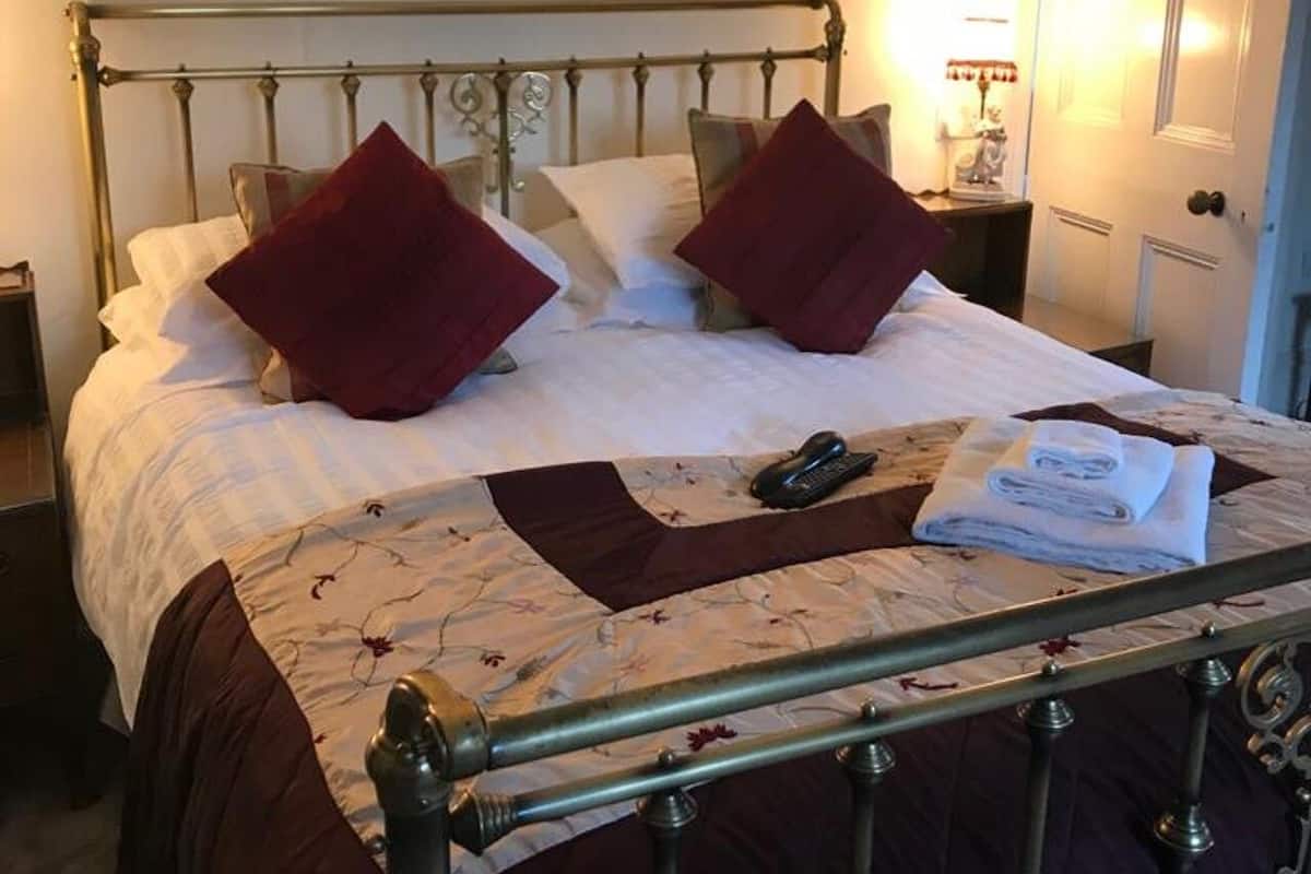 A neatly made bed with a metal frame, a bedside table with a lamp, and a door in the background.
