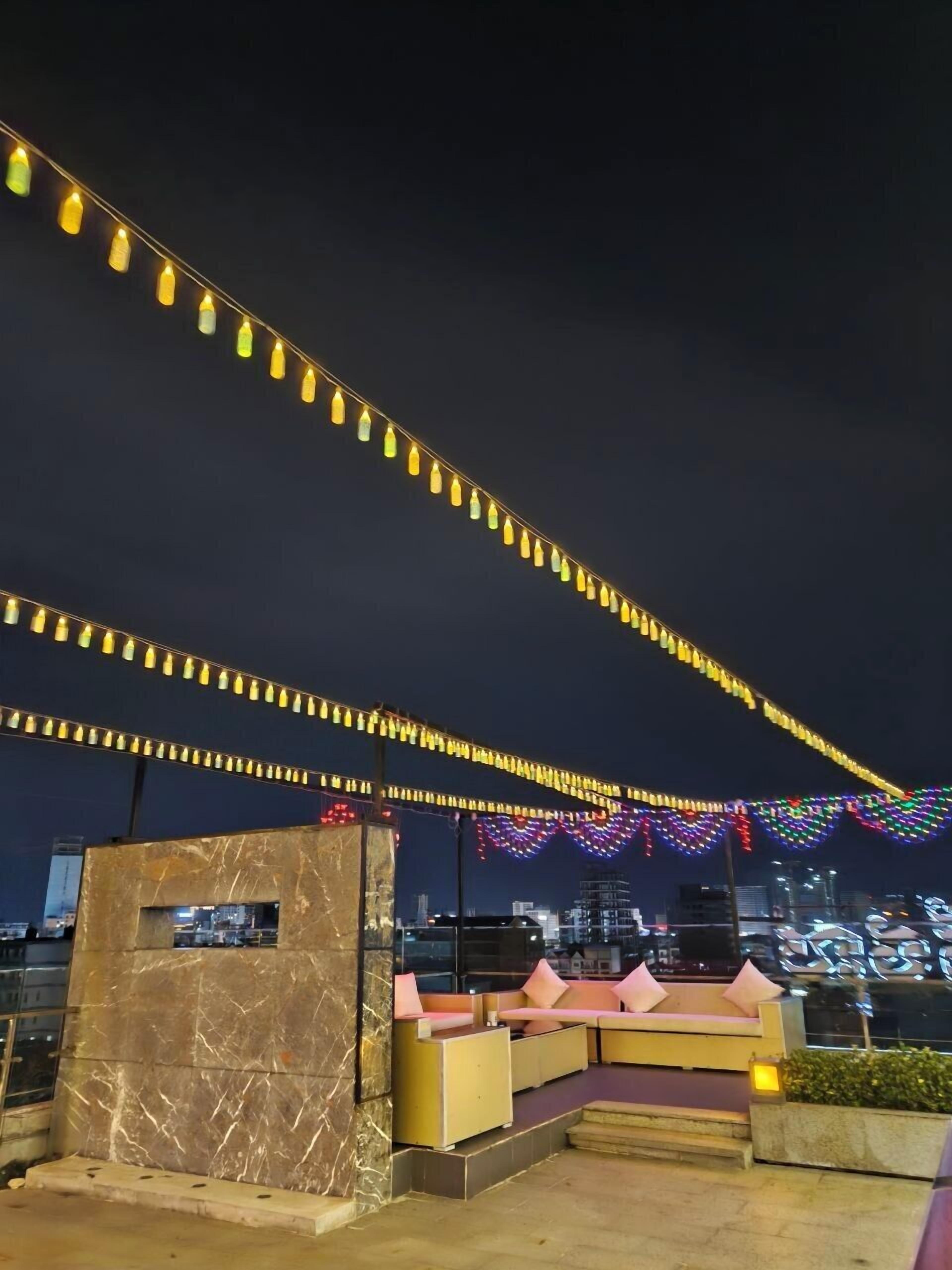 A rooftop terrace with a marble wall, outdoor seating, and string lights.