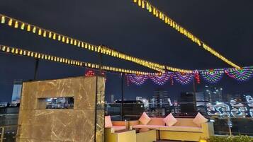 A rooftop terrace with a marble wall, outdoor seating, and string lights.
