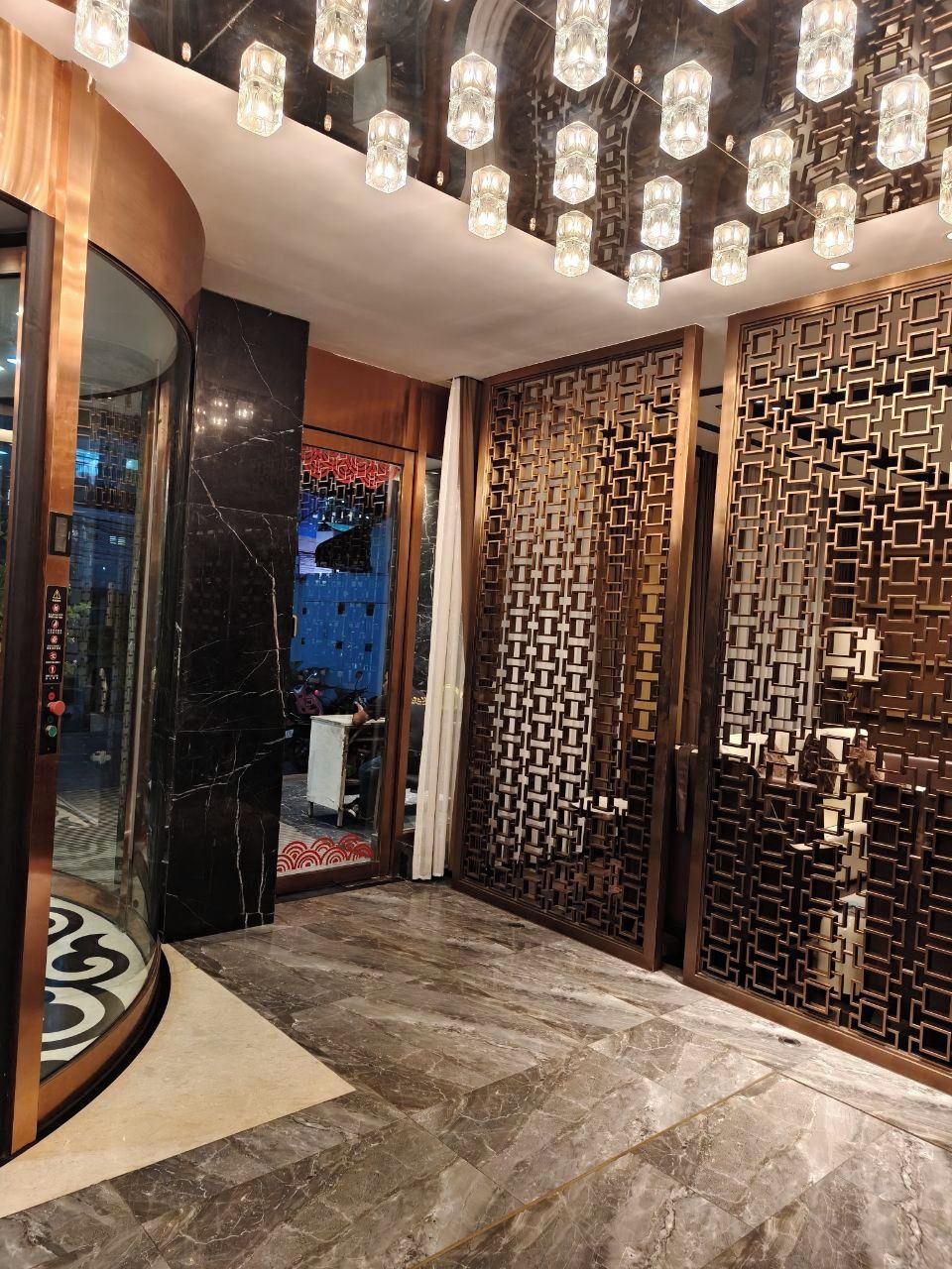Een modern interieur met een glazen lif met gebogen vormen, een houten wand met een patroon en een marmeren vloer.