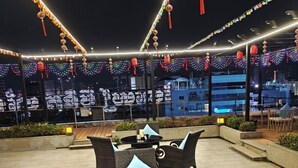 Un espace extérieur aménagé avec des meubles et des tables en osier, décoré de guirlandes lumineuses colorées et d’ornements suspendus.