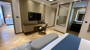 Une chambre d’hôtel moderne avec un plancher en bois, un téléviseur à écran plat fixé au mur, un bureau avec une chaise, un grand miroir et un lit recouvert d’une courtepointe à rayures bleues et blanches.
