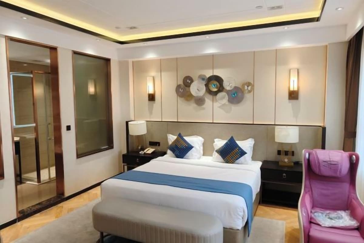 Habitación de hotel con una cama grande, mesitas de noche, una silla y un adorno en la pared.
