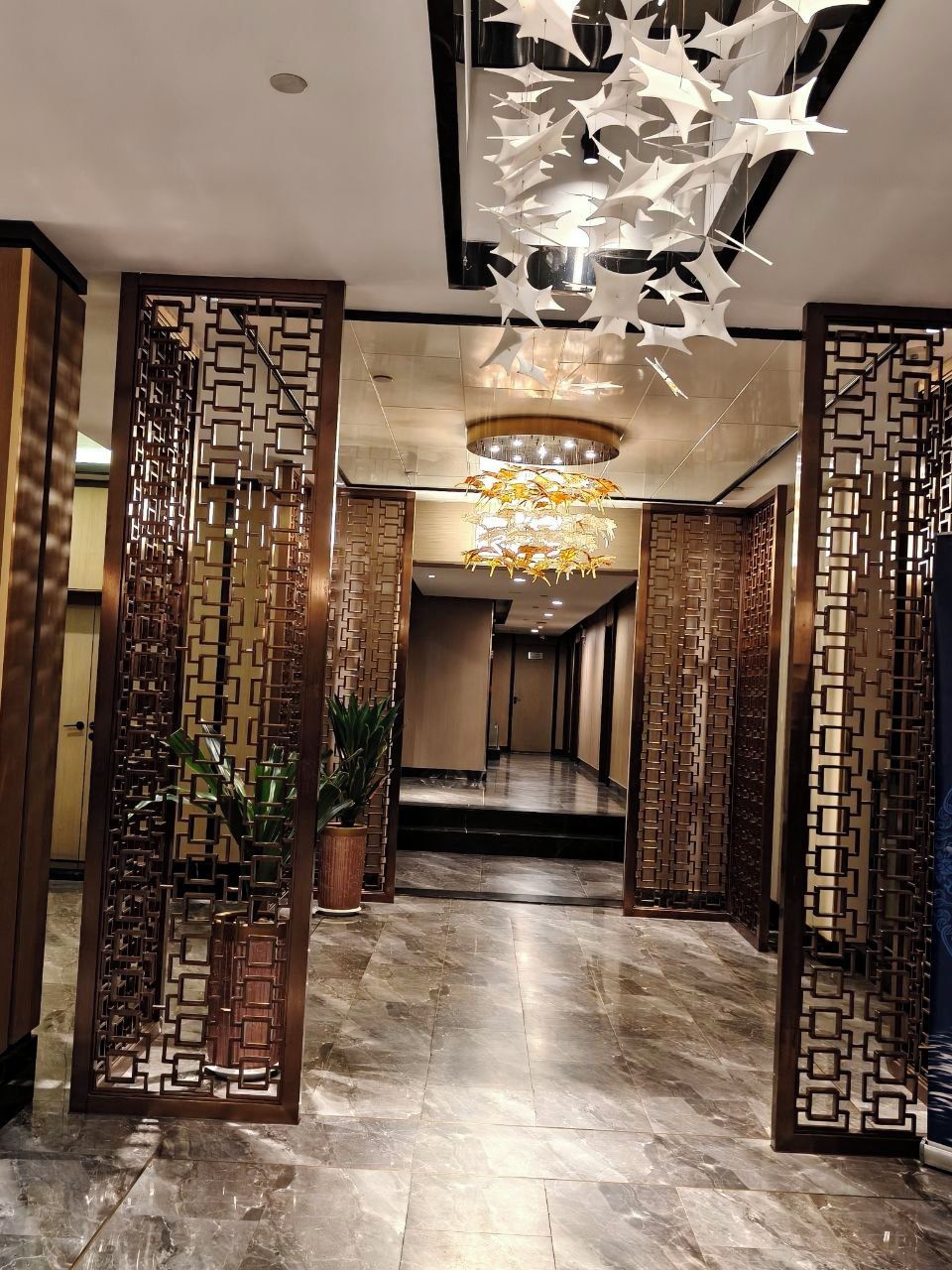 A hallway with a modern chandelier, decorative panels, and a marble floor.
