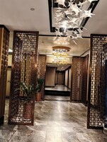 A hallway with a modern chandelier, decorative panels, and a marble floor.