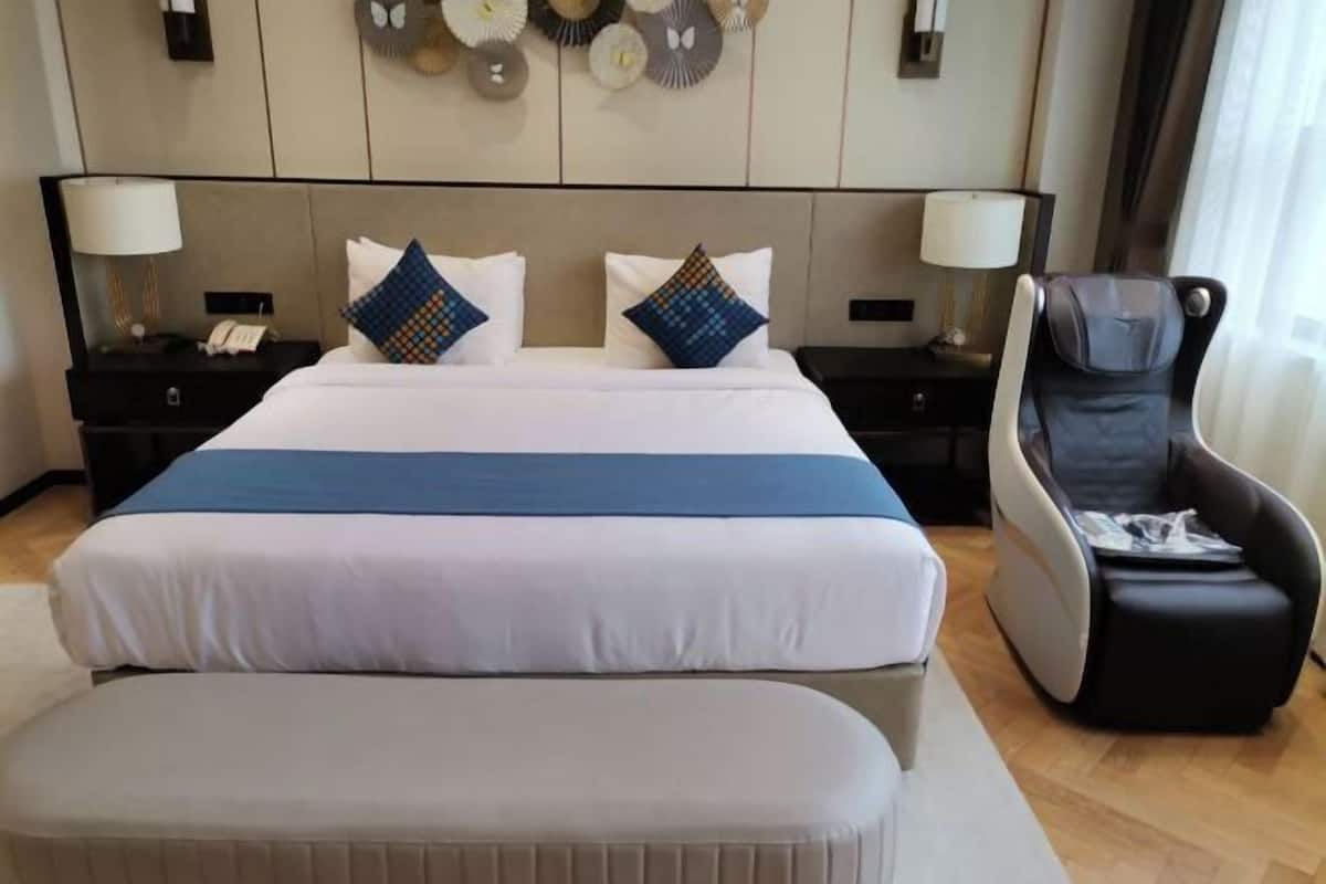 Habitación de hotel con una cama grande, dos mesitas de noche con lámparas, una silla de masaje y un reloj de pared.
