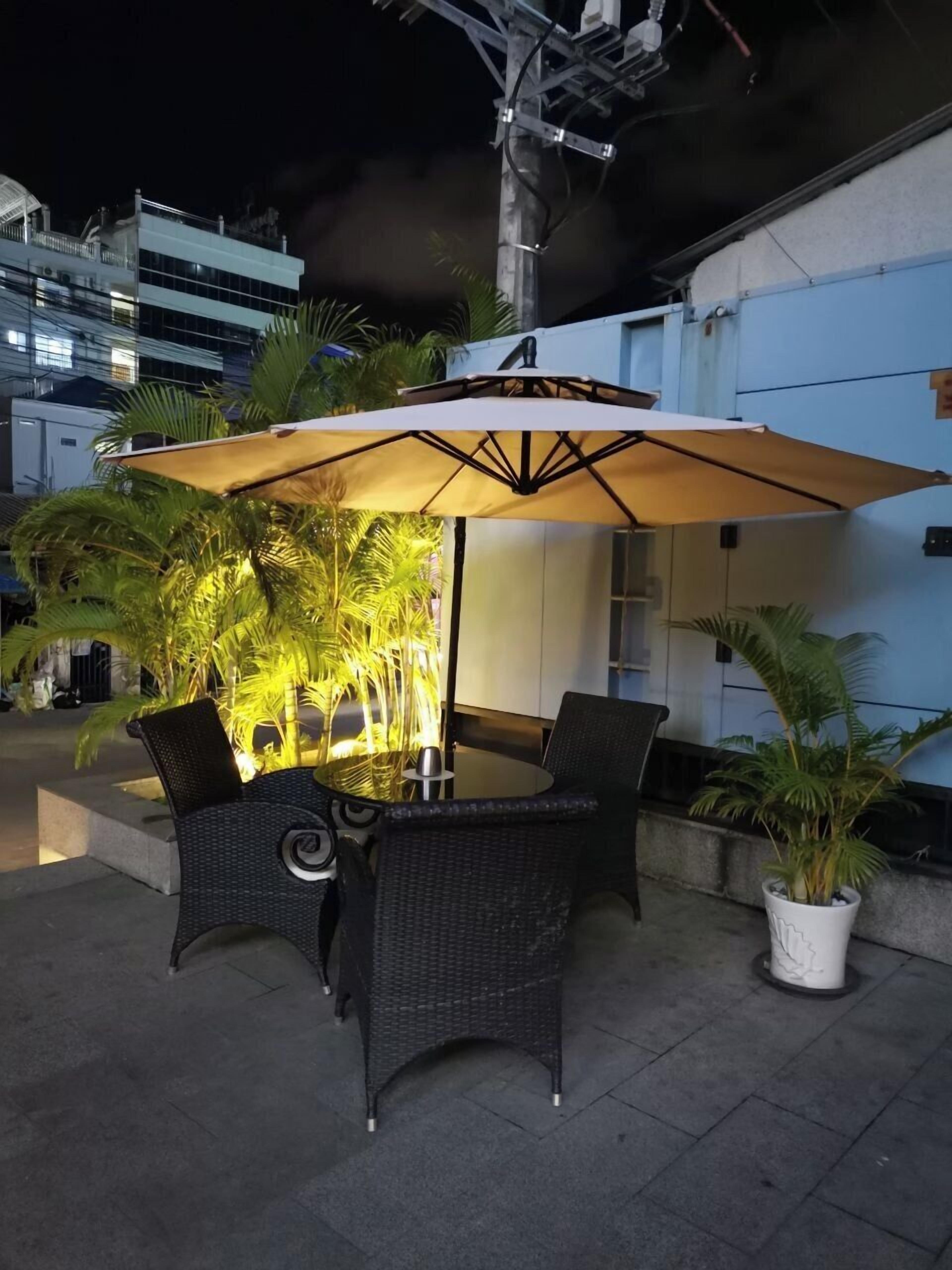 Un patio al aire libre con una mesa y sillas, rodeado de macetas con plantas y un paraguas grande.