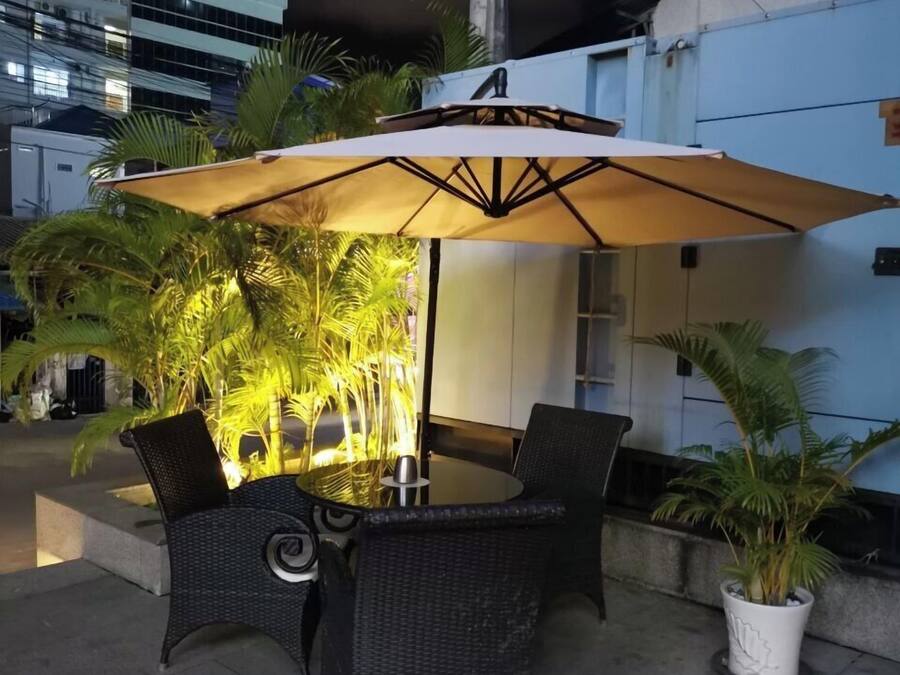 Un patio al aire libre con una mesa y sillas, rodeado de macetas con plantas y un paraguas grande.