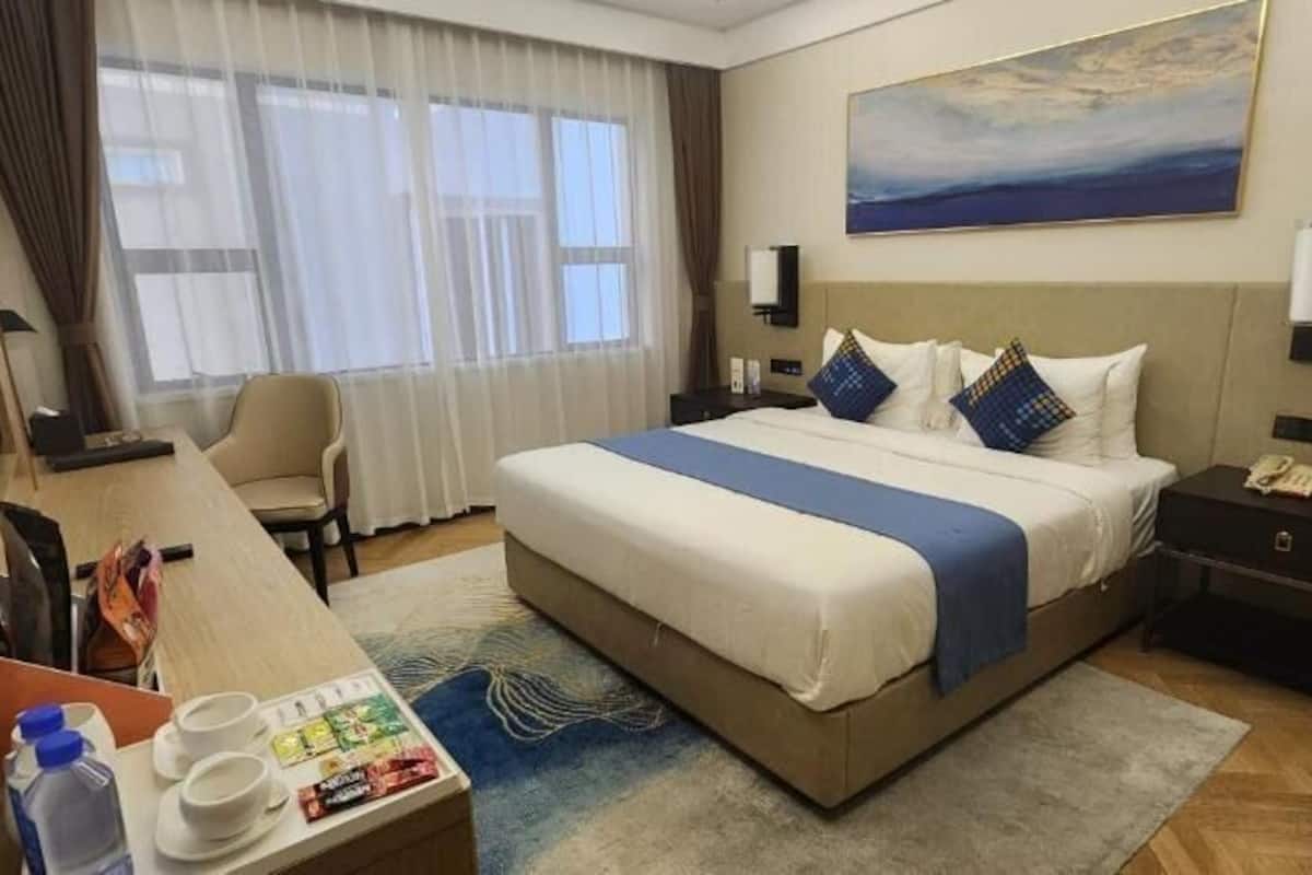 Habitación de hotel con una cama grande, un escritorio con silla, una mesita de noche y una ventana con cortinas.