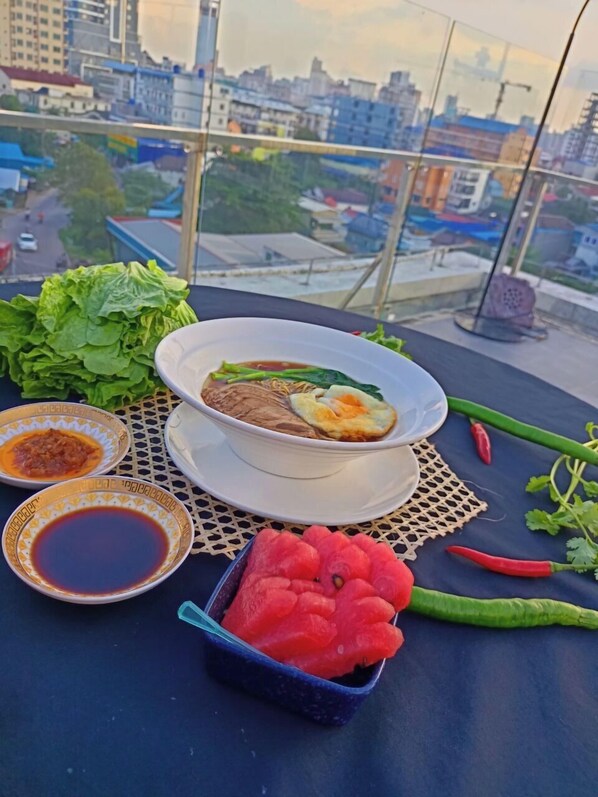 A meal with soup, noodles, and egg on a table with a city view. - Ocean Delight Boutique Hotel (Sihanoukville)