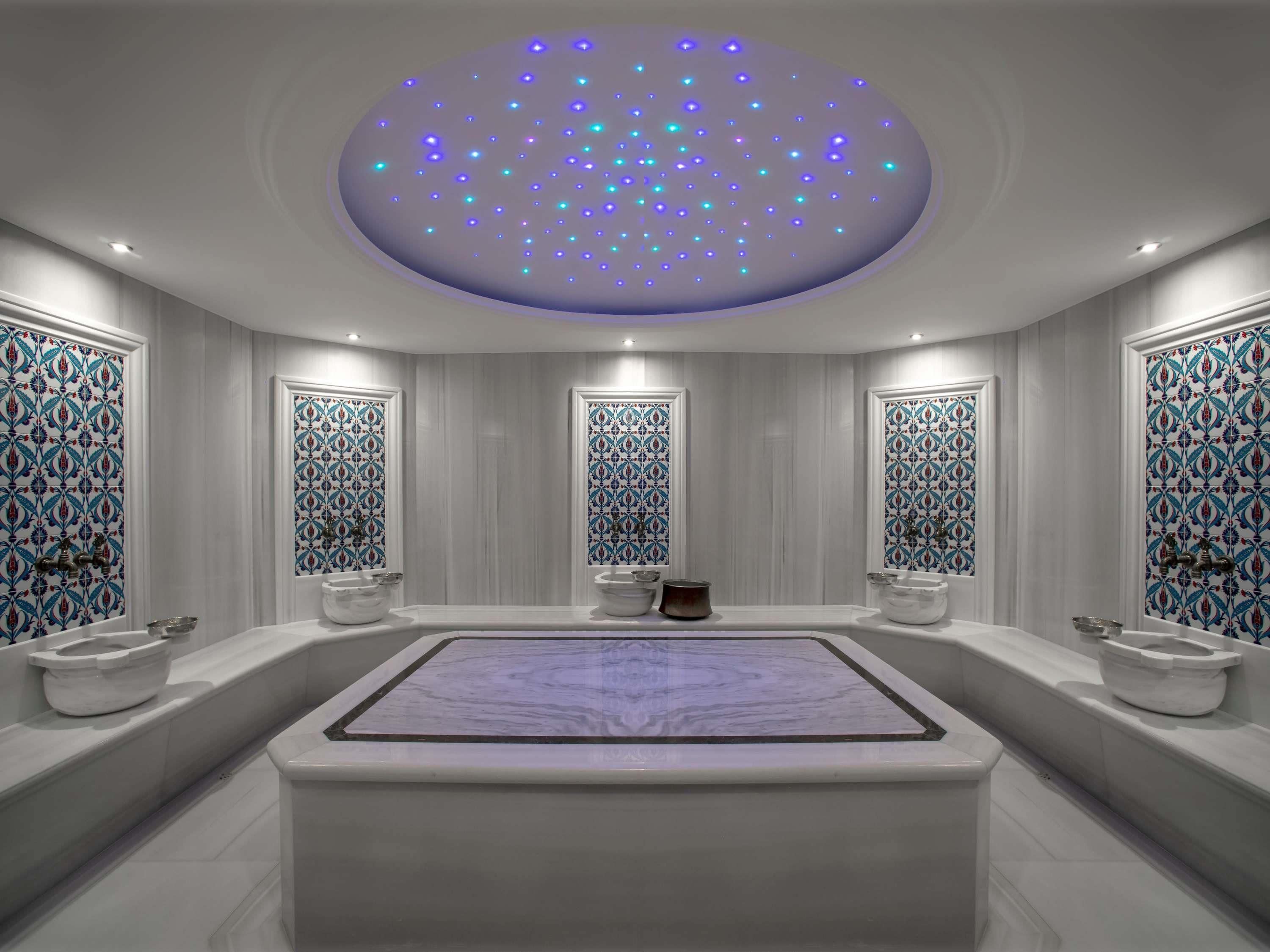 A modern bathroom with a large bathtub, two sinks, and a ceiling with blue LED lights.
