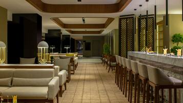 A modern hotel lobby with a bar area, sofas, and a dining setup.