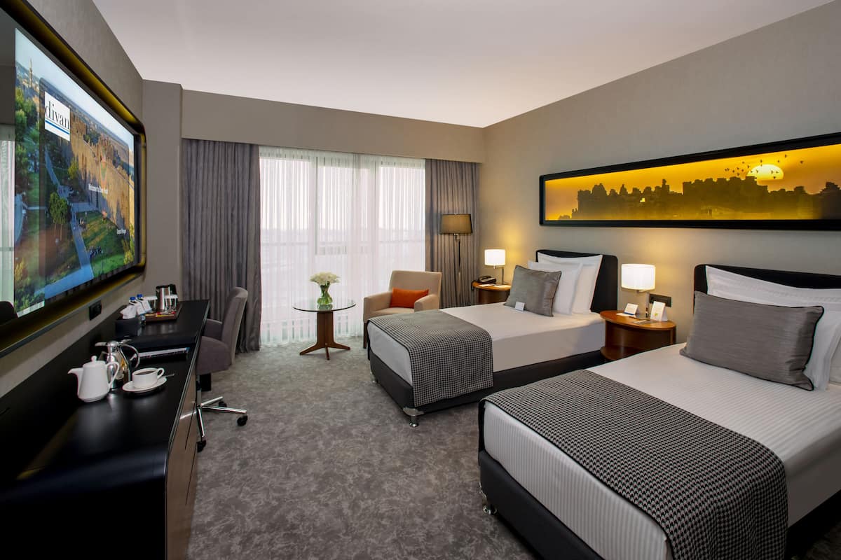 A hotel room with two beds, a desk, a chair, a TV, and a painting of a sunset.