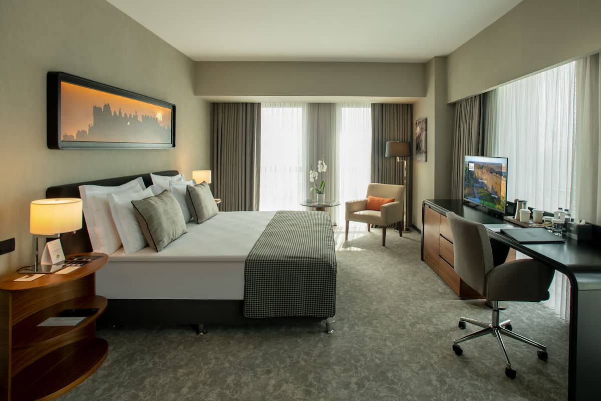 A hotel room with a bed, desk, chair, and TV.