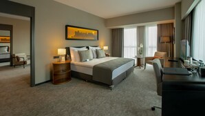 A hotel room with a large bed, a desk, a chair, a nightstand, and a painting on the wall. - Mövenpick Diyarbakir (Diyarbakir)