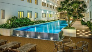 A swimming pool with a tiled deck, surrounded by lush greenery and a row of windows. - Green Residences (Manila)
