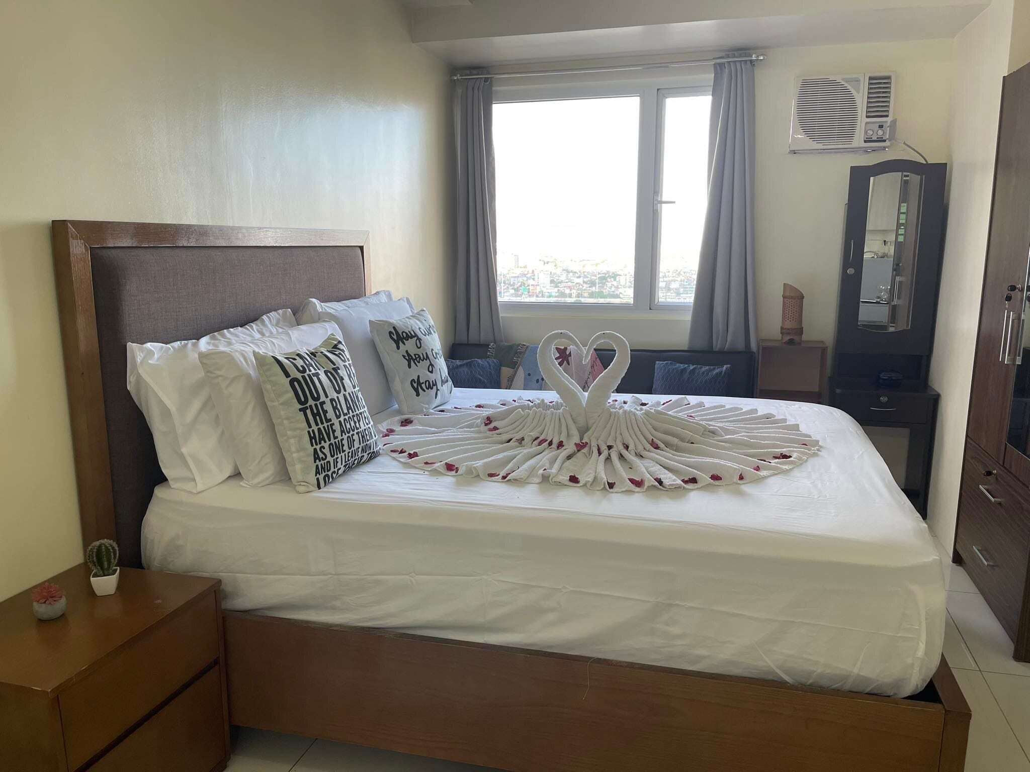 A neatly made bed with decorative pillows, a wooden headboard, and a swan-shaped towel arrangement.