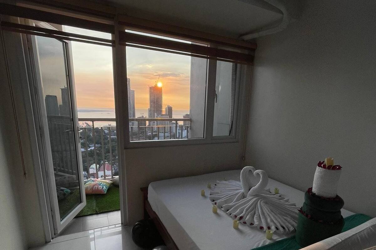 Un cuarto de hotel con una cama, vista al atardecer y un balcón.