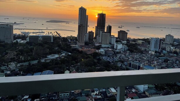 A cityscape with a prominent building in the foreground and a sunset over the water. - Green Residences (Manila)