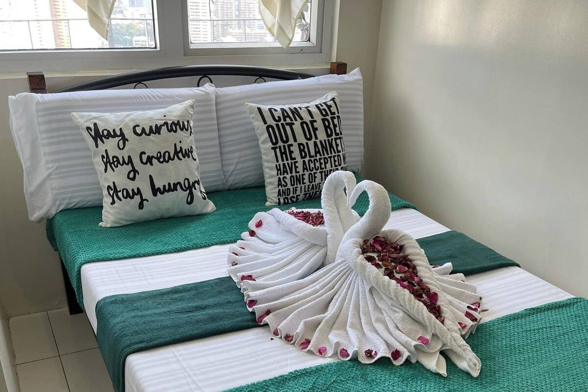 Habitación de hotel con dos camas, cada una con ropa de cama verde y blanca, y almohadas decorativas con citas motivacionales.