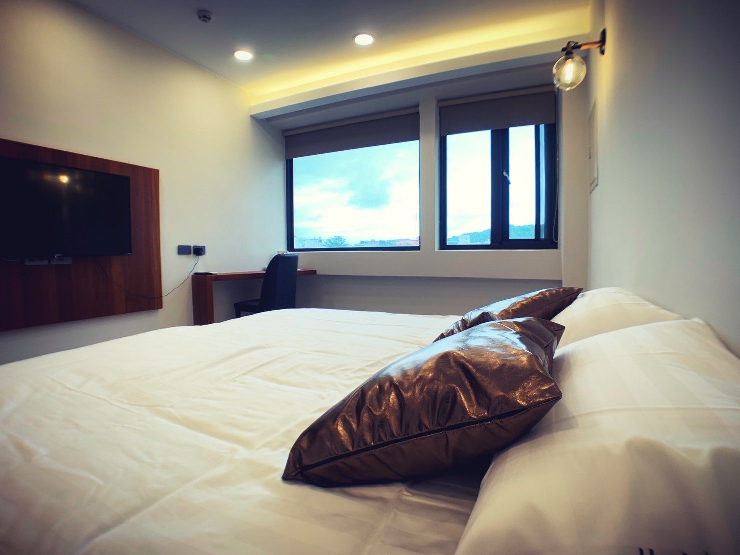 A modern hotel room with a large bed, a desk, and a TV mounted on the wall.