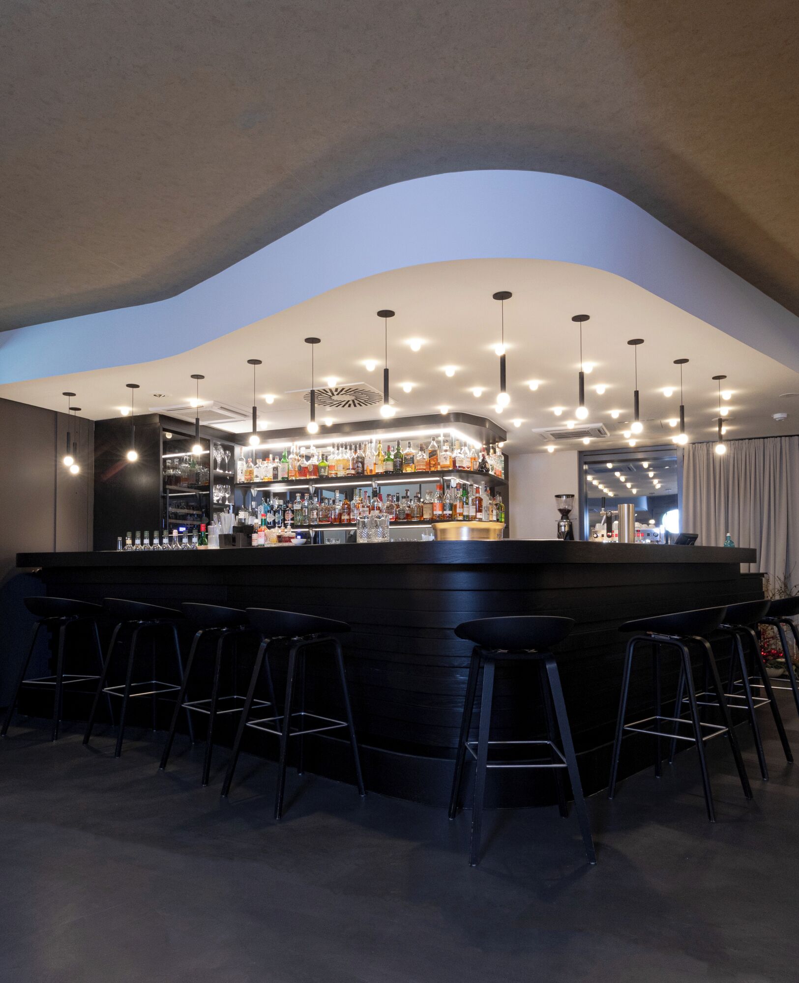 Un área de bar con techo curvo, varias luces colgantes y una variedad de botellas y vasos en estanterías.