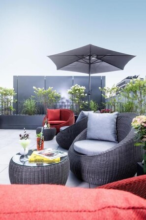 A modern outdoor seating area with wicker furniture, a red chair, and a large umbrella. - KPM Hotel & Residences Berlin, a Member of Design Hotels (Berlin)