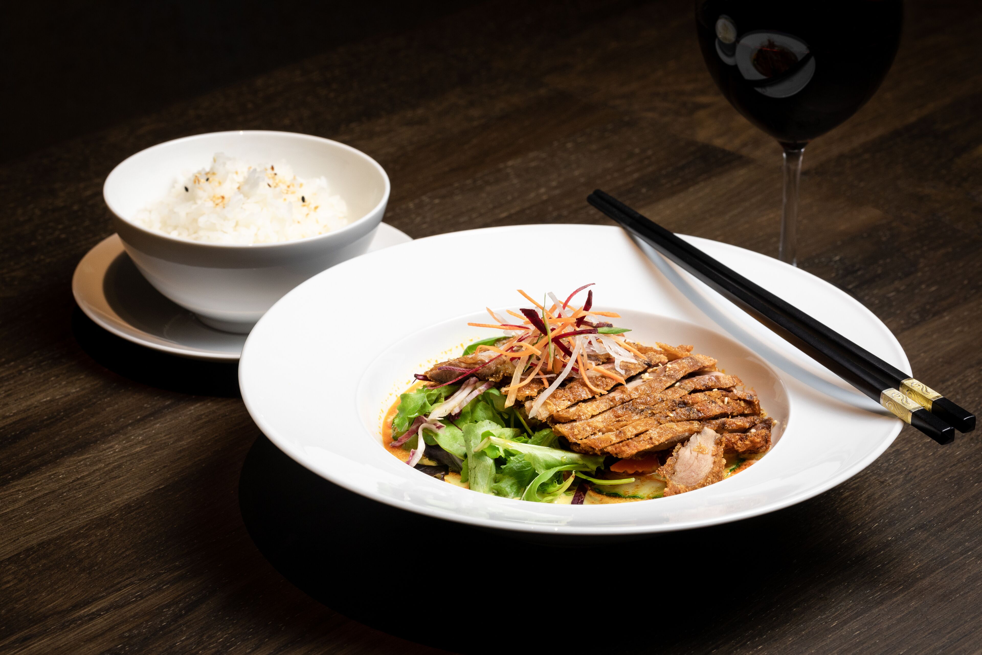 A bowl of rice and a dish with meat and vegetables on a wooden table.