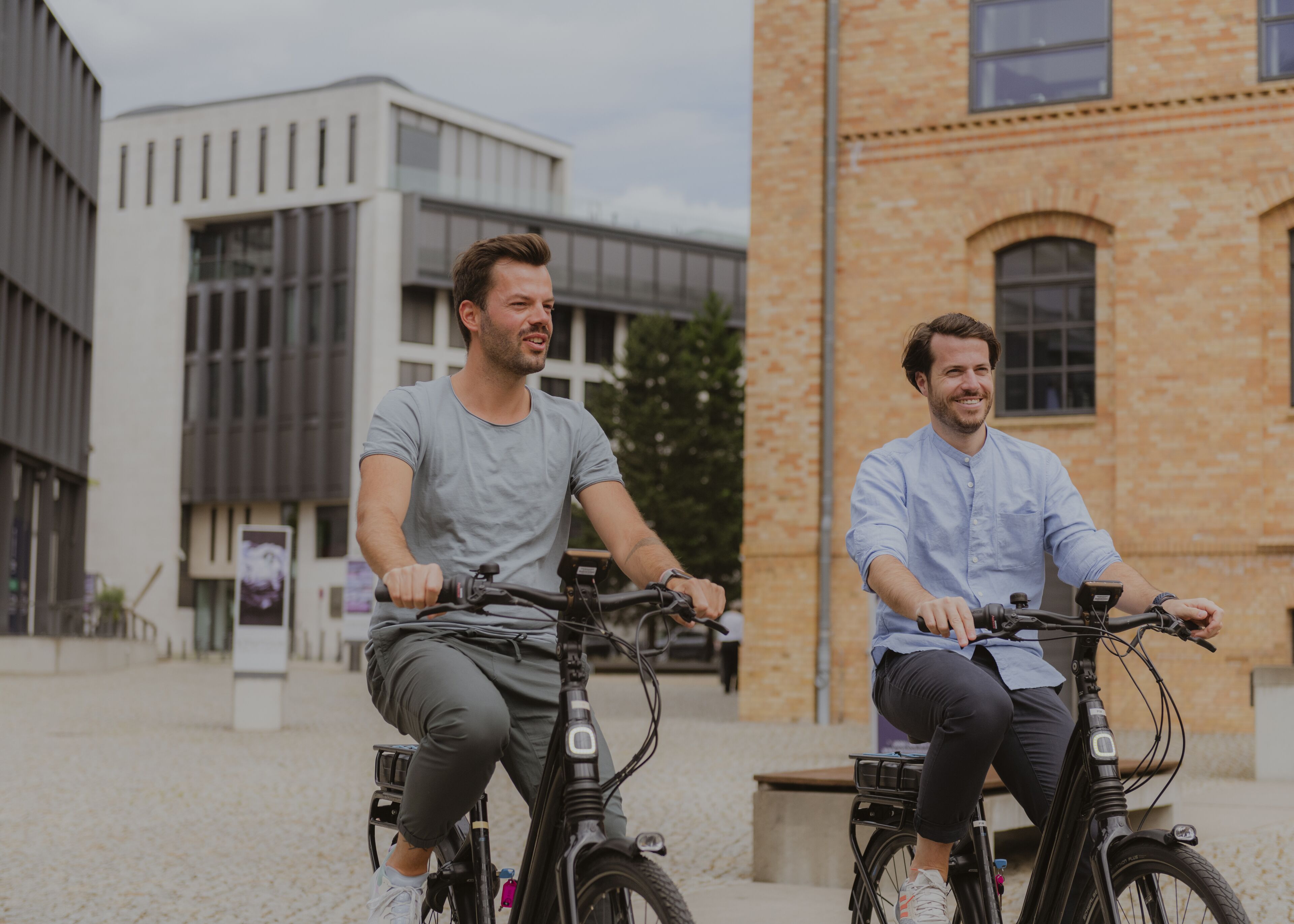 Dos personas andando en bicicleta por un camino adoquinado, con edificios modernos al fondo.