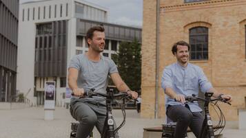 Dos personas andando en bicicleta por un camino adoquinado, con edificios modernos al fondo.