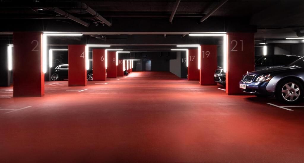 Un estacionamiento subterráneo de varios niveles con pilares iluminados y piso rojo.