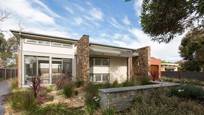 A modern two-story house with a stone facade, large windows, and a landscaped garden with various plants and a stone wall. - Douglas Hide and Sea (COWES)
