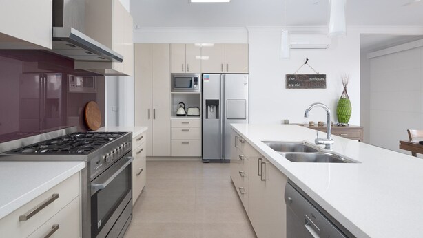 A modern kitchen with stainless steel appliances, white cabinetry, and a large island with a sink. - Douglas Hide and Sea (COWES)
