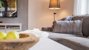 A modern living room with a grey sofa, striped pillows, a wooden bowl with apples, a white table, and a floor lamp. - Triumph in der Heide (Buchholz (Aller))