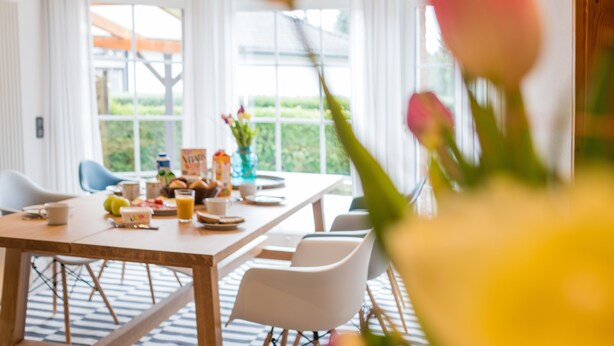 A dining area with a table set for breakfast, chairs, and a window with a view of greenery. - Triumph in der Heide (Buchholz (Aller))