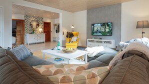 A modern living room with a sofa, a yellow armchair, a coffee table, and a flat-screen TV mounted on the wall. - Triumph in der Heide (Buchholz (Aller))
