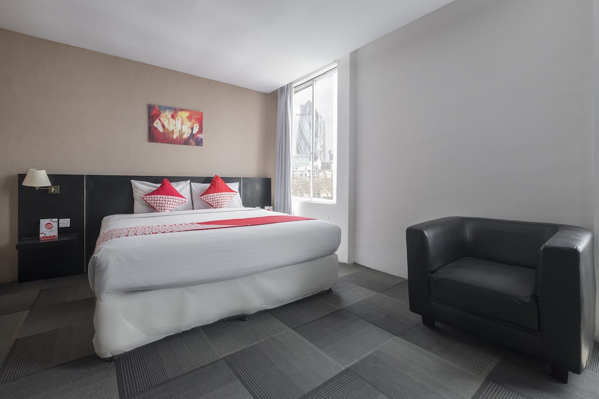 Ein Hotelzimmer mit einem großen Bett, einem schwarzen Ledersessel, einem Nachttisch mit Lampe und einem Gemälde an der Wand.