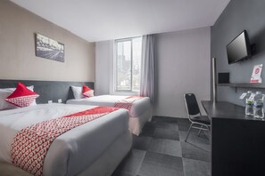 A hotel room with two beds, a desk, a chair, a TV, and a window with a city view. - Capital O 472 Hotel Asyra (Makassar)