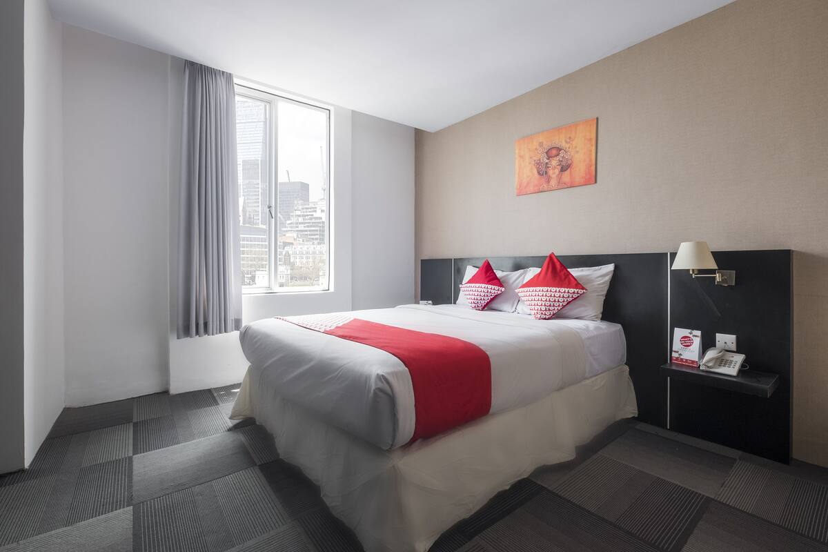 Ein Hotelzimmer mit einem großen Bett, einem Nachttisch, einem Telefon und einem Fenster mit Vorhängen.