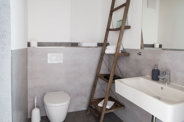 Un baño con un lavabo blanco, un inodoro y una escalera de madera apoyada en la pared.