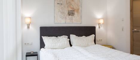 A neatly made bed with a white duvet, two bedside lamps, and a wall-mounted artwork.