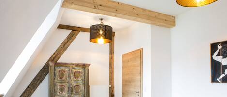 Una habitación tipo loft con techo inclinado, un mueble de madera con diseños intrincados, un sofá rosa y una lámpara colgante moderna.
