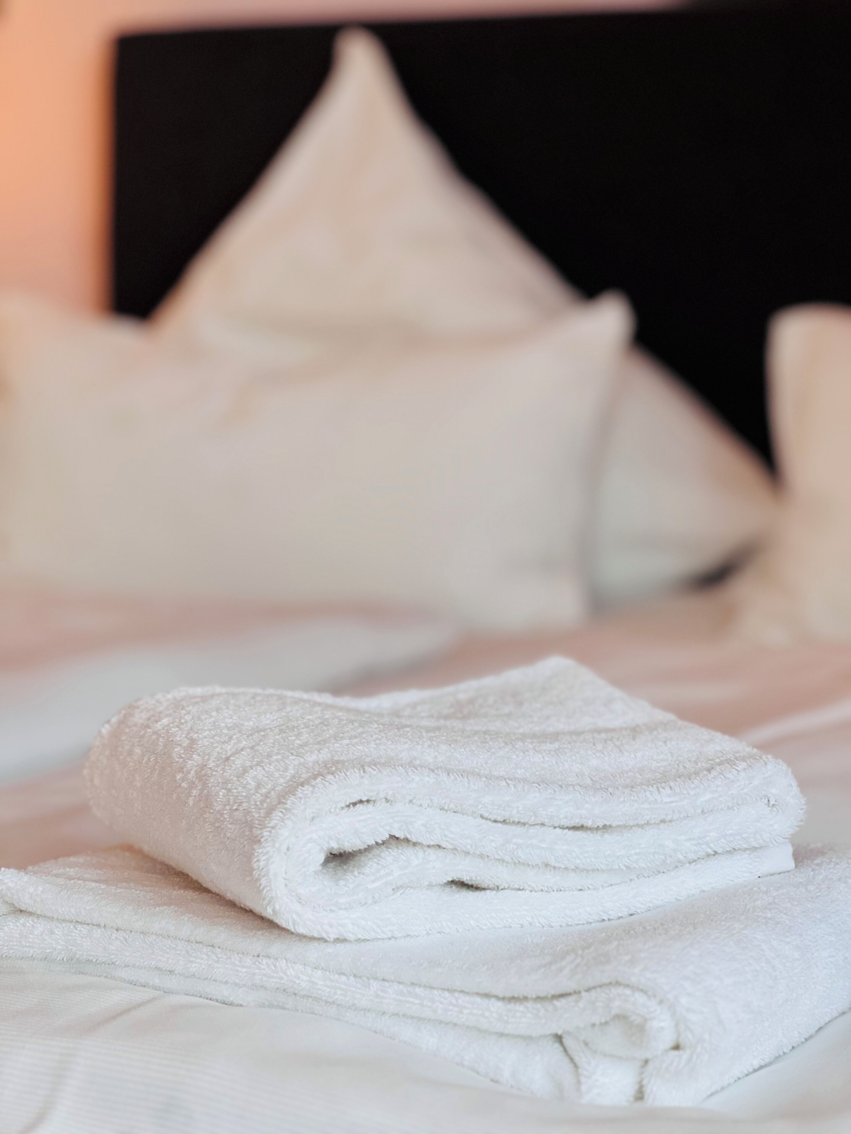 A neatly folded white towel on a bed with a black headboard and white pillows.