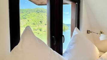 A bedroom with a large window, white pillows, and a view of a green landscape.