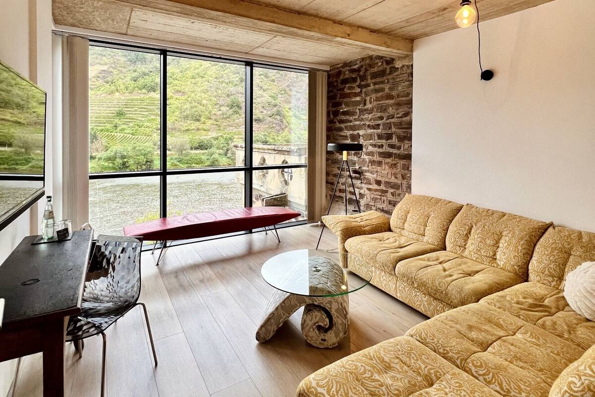 A spacious living area with a large window, a stone wall, and a cozy sofa.