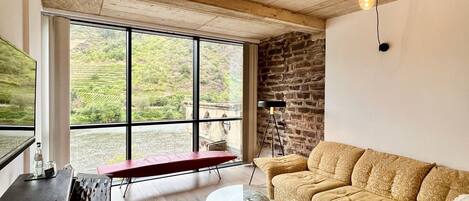 Un vaste espace de vie agrémenté d’une grande fenêtre, d’un mur en pierre et d’un canapé confortable.